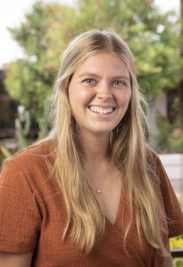 Headshot of Morgan Crump with blurred tree in background. Morgan is wearing a dark orange shirt. 
