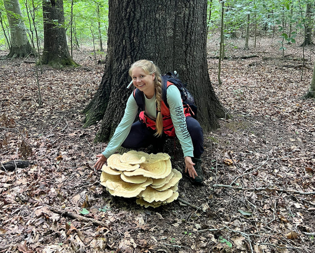 Photo of Daria Maslyukova in the forest behind a large fungus